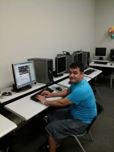 Young man with a bright blue shirt sitting at a computer in the computer classroom.
